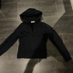 Stone island zip hoodie  - Säljer nu denna snygga Stone island zip hoodien. Den är i ett hyfsat bra skick. Inget problem med zip hoodien men den är lite solblekt men inget jag riktigt tänkt på när jag haft på mig den! Den är gjord i ett skönt matrieal och är riktigt snygg. Med mera frågor så är de bara att skriva! 