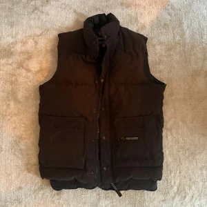 Canada Goose väst  - Snygg och varm svart dunväst från Canada Goose med dragkedja och knappar. Perfekt för kyliga dagar.  Retro väst från Canada goose, ny pris 2000kr.                  Storlek XS Pris 599kr