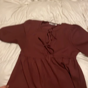 Vinröd klänning med knytband - Säljer en söt vinröd klänning med knytband framtill. Tröjan har trekvartsärmar och en mjuk material. Perfekt för höst och vinter med sin varma färgton.