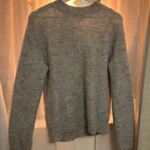Grå stickad tröja - Mysig grå stickad tröja med rund hals och långa ärmar. Perfekt för kyliga dagar och ger en stilren look. Passar bra till både jeans och kjol.