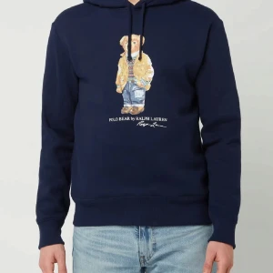 Mörkblå hoodie med björnmotiv från Ralph Lauren - Säljer en snygg mörkblå hoodie från Ralph Lauren med ett ikoniskt björnmotiv på framsidan. Skicka är 9/10 så den är använd ett fåtal gånger. Hör gärna av er vid frågor!