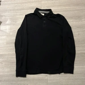 Svart långärmad pikétröja från Pier One - Snygg svart långärmad pikétröja från Pier One med klassisk krage och knappar framtill. Perfekt för en stilren look.