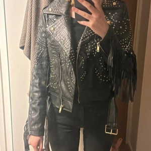 Svart skinnjacka med nitar och fransar - Snygg svart skinnjacka med coola nitar och fransdetaljer. endast använd få gånger. Köpt i London