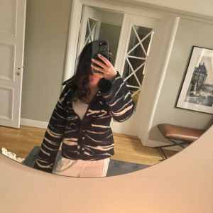 Svart och beige mönstrad jacka - Säljer en cool svart och beige jacka med ett unikt mönster. Jackan har långa ärmar och stängs med knappar. Perfekt för att ge din outfit en extra edge!