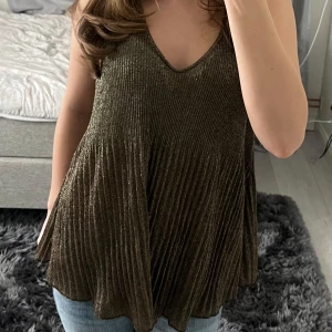 Glittrig guld/brun topp från MQ (Koul Edition) - Säljer en glittrig guldig/brun topp från MQ (Koul Edition) då den är för stor på mig. Toppen har en v-ringad design och är ärmlös med lös passform och strechigt tyg. Perfekt för att lägga till lite glitter i garderoben eller inför nyår🎉