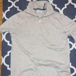 Beige tröja med dragkedja från Jack & Jones - Säljer en stilren beige tröja från Jack & Jones med dragkedja vid halsen. Perfekt för en avslappnad look. Tröjan har långa ärmar och en mjuk känsla.