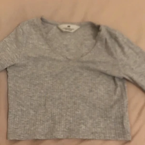 Grå ribbad topp från H&M - Säljer en grå ribbad topp från H&M med lång ärm och rund halsringning. Perfekt för en avslappnad stil. Toppen är i storlek 134/140 och har en mjuk och bekväm känsla.
