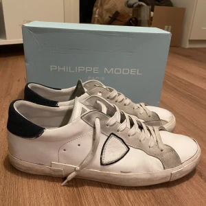 Vita sneakers från Philippe Model - Snygga vita sneakers från Philippe Model med grå och mörkblå detaljer. Skorna har en klassisk design med snörning och en bekväm passform. Perfekta för en stilren look. Box medföljer och skorna är i toppskick. Den enda defekten är som du ser på sista bilden men inget som man lägger märke till.     MVH Erik