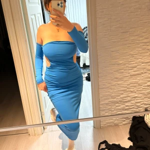 Blå one-shoulder klänning - Snygg blå one-shoulder klänning med cut-out detaljer i midjan. Klänningen har en tight passform och är lång, perfekt för en kväll ute. Den är tillverkad i ett stretchigt material som framhäver figuren. Passar perfekt för s/m/l storlek