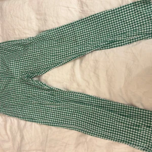 Gröna rutiga byxor från Øst London - Snygga gröna och vita rutiga byxor från Øst London. Perfekta för en trendig look med sin raka passform och bekväma midja. Passar utmärkt för både avslappnade och mer uppklädda tillfällen.