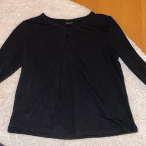 Svart kofta från Gina Tricot - Säljer en stilren svart kofta från Gina Tricot. Den har långa ärmar och en enkel knapp framtill. Perfekt för lager-på-lager-stil eller som ett lätt lager under kyliga dagar.