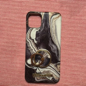 Marmormönstrat mobilskal från iDeal of Sweden (iPhone 11 PRO Max) - Snyggt marmormönstrat mobilskal från iDeal of Sweden med en stilren design i svart, vit och guld. Skalet passar en iPhone 11 PRO Max. Skalet har en praktisk ringhållare i guld som ger extra grepp och funktionalitet. Perfekt för att ge din telefon ett elegant utseende. Den har en liten spricka högst upp i en hörnet precis över kamran. Tror de hände när jag skulle ta av det då det är ett hårt skal men funkar fin. Lite slitage kan man se, men inget man tänker på. Pris går att diskutera😊od pris 475