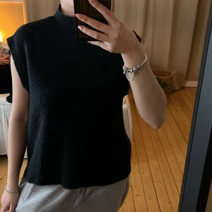 Svart ärmlös stickad topp - Snygg svart ärmlös stickad topp med hög krage. Perfekt för lager-på-lager eller som den är. Enkel och stilren design som passar till många olika outfits.