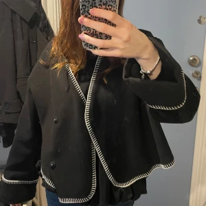 Svart kavaj med vita detaljer - Snygg svart kavaj med vita kontrastsömmar längs kanterna. Kavajen har en croppad passform och långa ärmar. Perfekt för en stilren look. Den är knappt använd och den är i jätte fint skick 💗