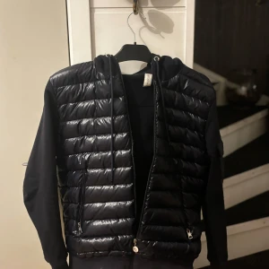 Moncler Cardigan (JUL REA) - Snygg blå cardigan från Moncler med dragkedja och huva. Jackan har långa ärmar och ett quiltat mönster på framsidan. Perfekt för kyligare dagar. Passar perfekt ovh har en bra passform. Dragkedjan är lite sönder men går o fixa hos skräddare för typ 200kr då ja kan dra ner priset om du väljer o fixa själv.