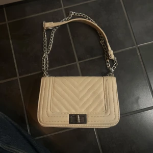Beige quiltad axelväska med kedja - Snygg beige axelväska med quiltat mönster och silverfärgad kedja. Använd ett fåtal gånger, snygg och stilren. Nyskick. 