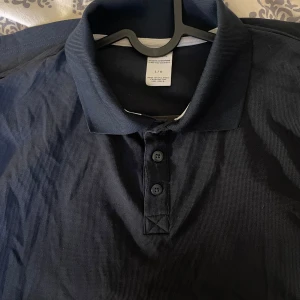Mörkblå pikétröja från Helly Hansen - Säljer en stilren pikétröja från Helly Hansen. Tröjan har en klassisk krage med tre knappar framtill. Perfekt för en avslappnad men ändå snygg look. Knappt använd, mycket bra skick🩷
