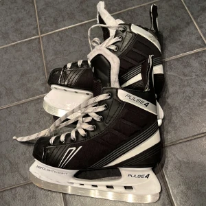 Svarta skridskor Pulse 4, Stl 37 - Säljer ett par svarta och vita skridskor från Pulse, modell 4. De har snörning och en vadderad insida. Använt skick, stl 37. 
