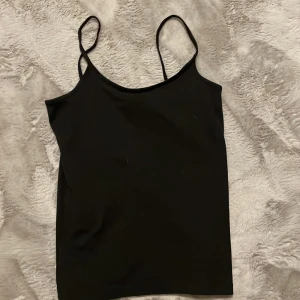 Svart linne från Åhléns  - Säljer ett stilrent svart linne med tunna axelband. Använt en gång nytt skick