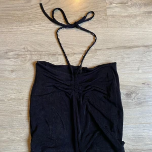 Svart axelbandslös tubtopp - Snygg svart axelbandslös tubtopp med knytband i nacken. Perfekt för en stilren look och kan enkelt matchas med olika outfits.