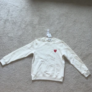 Vit tröja från Comme des Garçons - Säljer en stilren vit tröja från Comme des Garçons med det ikoniska röda hjärtat på bröstet. Tröjan har långa ärmar och en rund halsringning. Perfekt för en minimalistisk look. Aldrig använd pga dess storlek. Kan ta ner priset lite vid snabb köp