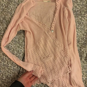 Ljusrosa oddmolly kofta med spetsdetaljer - Säljer en söt rosa stickad kofta med fina spetsdetaljer och knappar framtill. Koftan har långärmade ärmar och en unik design med små fickor.  Från Oddmolly strl s