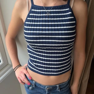 Randig ribbad topp från H&M - Säljer en superfin randig topp från H&M i storlek XS. Den är mörkblå med vita ränder och har en ribbad struktur. Toppen är ärmlös och croppad, perfekt för sommaren! Den är i nyskick och har aldrig använts, och har lappen kvar. köpt för 99kr. skriv för fler frågor eller bilder!