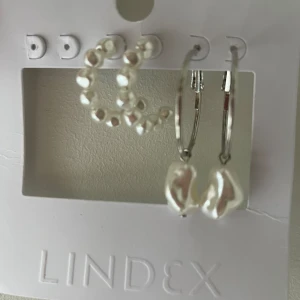 Örhängen från Lindex med pärlor - Säljer ett set med örhängen från Lindex. Setet innehåller två par örhängen:  ett par silverringar med vita pärlor och ett par silverringar med större vita pärlor som hänger. aldrig andvändna, och köpta för 129kr. skriv för fler bilder eller frågor!