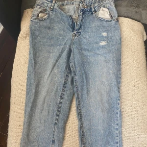 Blå jeans med slitningar - Säljer ett par blå jeans med slitningar på framsidan. De har en klassisk femficksdesign och en ljus tvätt. Jeansen är i en straight fit och ser ut att vara i välanvänt skick. 