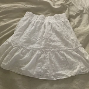 Vit kjol från Sister - Säljer en superfin vit kjol från märket Sister. Kjolen är i storlek S och har ett vackert broderat mönster. Den är kort och har en volangdetalj längst ner. Perfekt för sommaren eller en festlig tillställning! 🥰