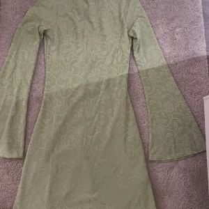 Ljusgrön klänning från NA-KD - Säljer en superfin ljusgrön klänning från NA-KD. Den har ett blommigt mönster och är långärmad. Klänningen har en öppen rygg med knytning.🌸