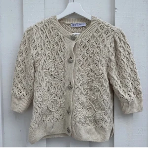 Beige stickad kofta från Zara - Säljer en superfin beige stickad kortärmad kofta från Zara, men köpt på plick. Den har ett fint mönster och blommiga knappar. Koftan har trekvartsärmar och är perfekt för höst och vår. Den är i nyskick och väldigt mysig att ha på sig. Passar både till vardags och fest! Bilderna är lånade från den tidigare säljaren. den har knappt använts sedan köpet. Storlek M men passar också S bra!