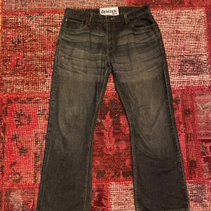 Mörkblå jeans från Denizen - Säljer ett par mörkblå jeans från Denizen. De är i bra skick och har en klassisk femficksdesign. Jeansen har en rak passform och är perfekta för vardagsbruk. De har en knapp och dragkedja framtill.