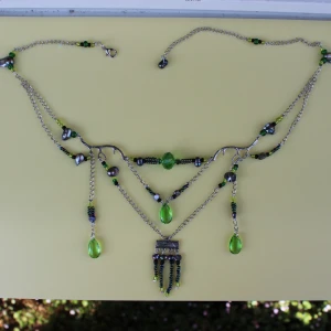 Grönt och silverfärgat halsband med pärlor - Säljer ett unikt halsband med flera lager och detaljer. Halsbandet har en silverfärgad kedja med gröna och svarta pärlor samt gröna droppformade hängen. Det finns också små silverfärgade hjärtan och andra detaljer som ger halsbandet en elegant och bohemisk känsla. Perfekt för att piffa upp en outfit till fest eller vardag!