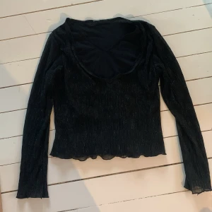 Svart glittrig långärmad topp - Säljer en snygg svart topp med glittriga detaljer. Den är långärmad och har en v-ringad hals. Perfekt för festliga tillfällen! Toppen är i bra skick och har en tight passform.