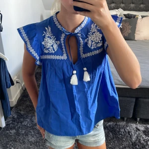 Blus  - Blå blus från H&M med vackert broderi på och snören med tofsar man kan knyta eller lämna öppet💙 Aldrig använd, jättebra skick!  Pris kan alltid diskuteras❣️