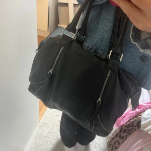 Väska  - Svart väska i skinnmaterial med silvriga detaljer. Vet ej vart den är köpt. Hör av dig vid frågor<3 Väskan har lite defekter!