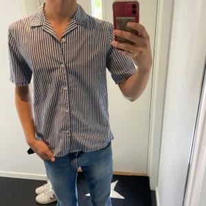 Bläck skjorta - Kortarmad skjorta från bläck. Blå vit randig. Modellen är 180cm 63kg. Skriv vid funderingar 💬 