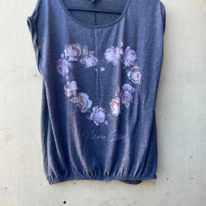 Grå topp med blommönster från Amisu - Säljer en grå topp från Amisu med ett vackert blommönster i form av ett hjärta på framsidan. Toppen är ärmlös och har en rund halsringning. Perfekt för en avslappnad stil!