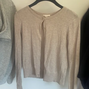 Beige kofta från Basic - Säljer en stilren och enkel beige kofta från Basic. Den är i storlek XS och har långa ärmar. Koftan är gjord i ett mjukt material och har knappar framtill. Perfekt för både vardag och lite kyligare dagar.