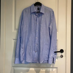 Ljusblå skjorta från BOSS - Säljer en stilren ljusblå skjorta från BOSS i storlek L. Skjortan har en casual fit och är perfekt för både vardag och fest. Helt ny aldrig använd köpt för 1999 på Jonhells påse finns.