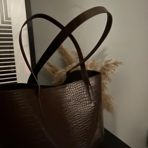 Handväska  - Hej! Säljer nu denna fina och stilrena handväskan. Det är en brun snygg färg och materialet är lite glansigt. Väskan har aldrig kommit till använd där av väldigt bra skick🌸