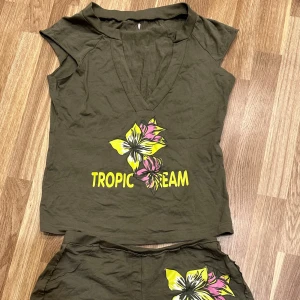 Grön topp med tropiskt tryck - Ett set med en grön topp och shorts. Toppen har en djup v-ringning och är ärmlös, perfekt för sommarens varma dagar. Materialet är i bomull. Osäker på storleken men skulle säga S/M! 