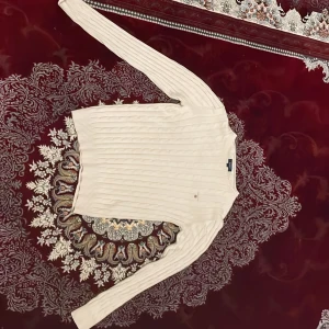 Beige stickad tröja från GANT - Säljer en superfin beige stickad tröja från GANT. Den har ett klassiskt kabelstickat mönster och är perfekt för både höst och vinter. Tröjan är långärmad och har ribbade muddar vid ärmslut och nederkant. Den är i storlek S och i nyskick. Perfekt för en stilren och mysig look!