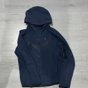 Blå nike tech - Säljer min använda nike tech för den är nu för liten. Den har några små skador men inte så många, lite vid fickorna och liten skada på vänstra axeln men inget stort. Pis kan ändras men inte under 150