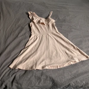 Beige klänning med volangdetalj - Säljer en superfin beige/rosa klänning med volangdetalj vid axlarna. Den är ärmlös och har en luftig passform, perfekt för sommarens alla fester. Klänningen är i ett mjukt och bekvämt material som känns skönt mot huden.