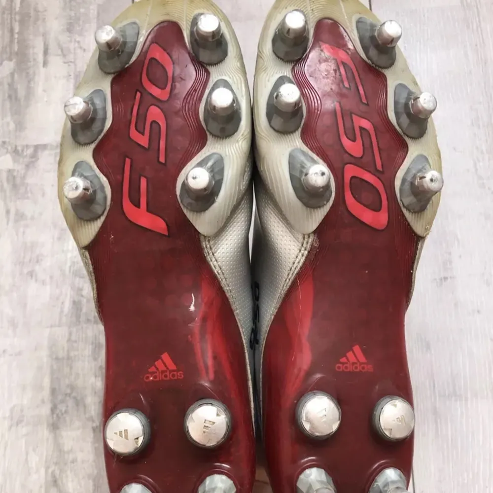 Säljer ett par klassiska Adidas F50 fotbollsskor i rött och silver. Skorna har en snygg design med röda detaljer och silverfärgade dobbar. Perfekta för fotbollsspel på gräsplaner.. Skor.