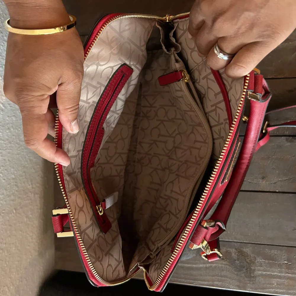 Säljer en snygg handväska från Calvin Klein i rött och brunt. Väskan har ett klassiskt monogrammönster och är gjord i syntetmaterial. Den har både handtag och en avtagbar axelrem, vilket gör den superpraktisk. Insidan är rymlig med flera fack och dragkedja för säker förvaring. Nyskick . Laukut & Käsilaukut.