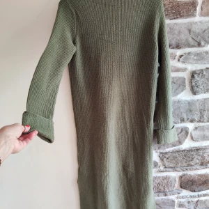 Olivgrön stickad klänning från Rainbow - Säljer en superfin olivgrön stickad klänning från Rainbow. Den har en skön och mysig känsla med långa ärmar och en liten slits på sidan för extra stil. Perfekt för höst och vinter när du vill vara både varm och snygg!