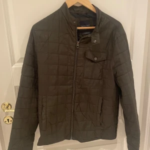 Olivgrön quiltad jacka från Zara Man - Säljer en snygg olivgrön quiltad jacka från Zara Man. Jackan har en dragkedja framtill och en knappdetalj vid kragen. Perfekt för höst och vår med sin stilrena design och bekväma passform. Den är i bra skick och redo för nya äventyr!